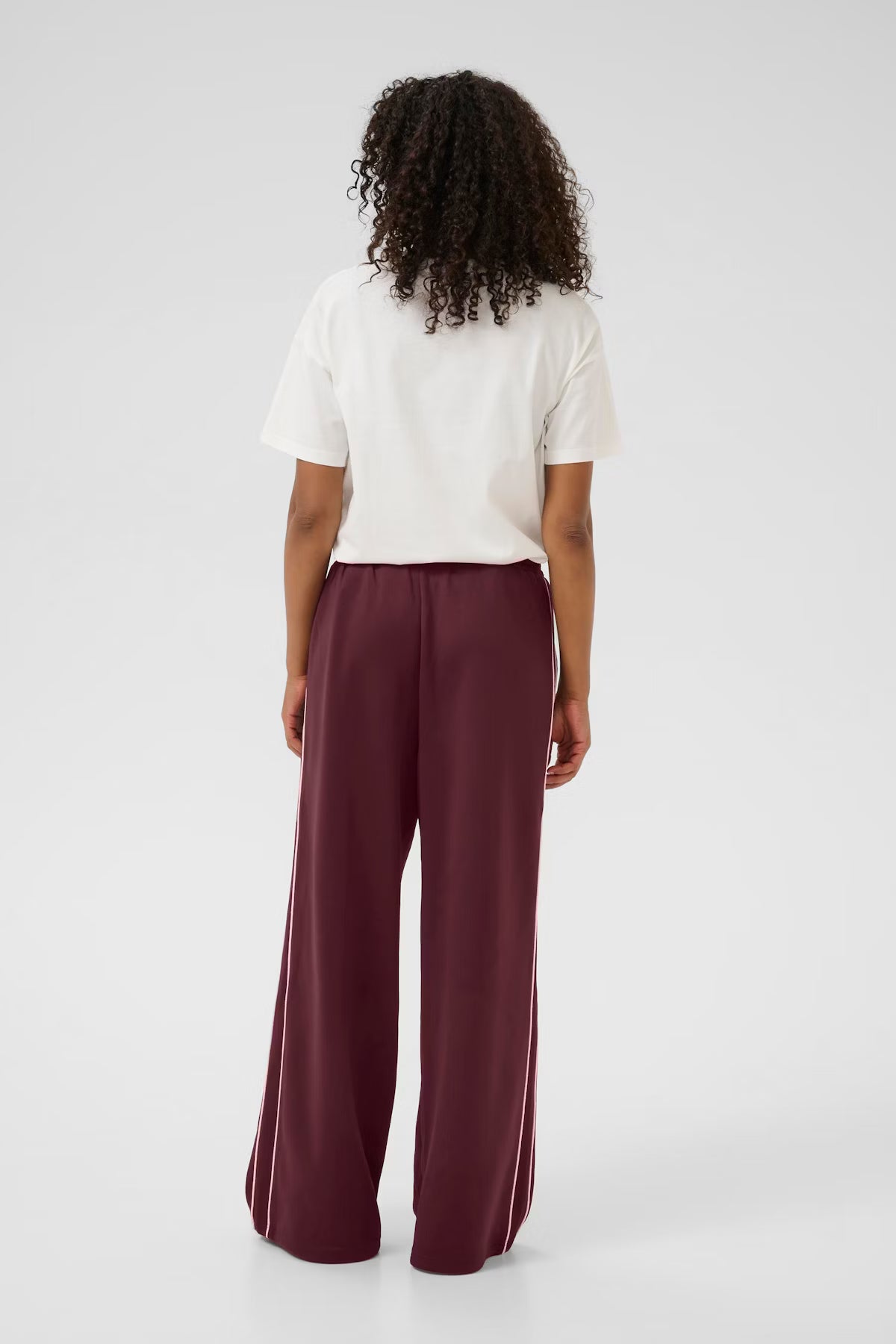 Person wearing a white shirt and burgundy pants on a light gray background