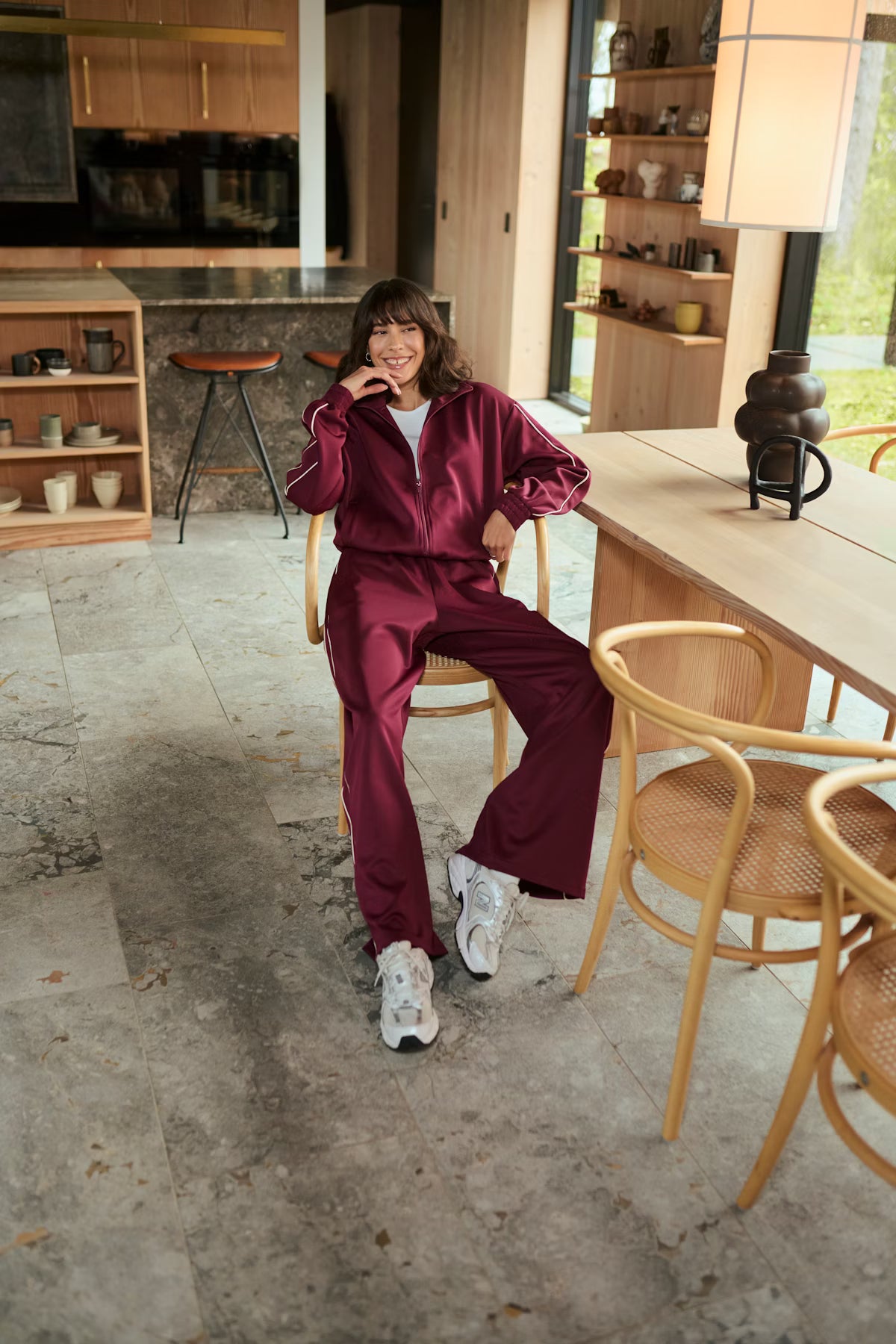 Person in a maroon tracksuit sitting in a modern kitchen.