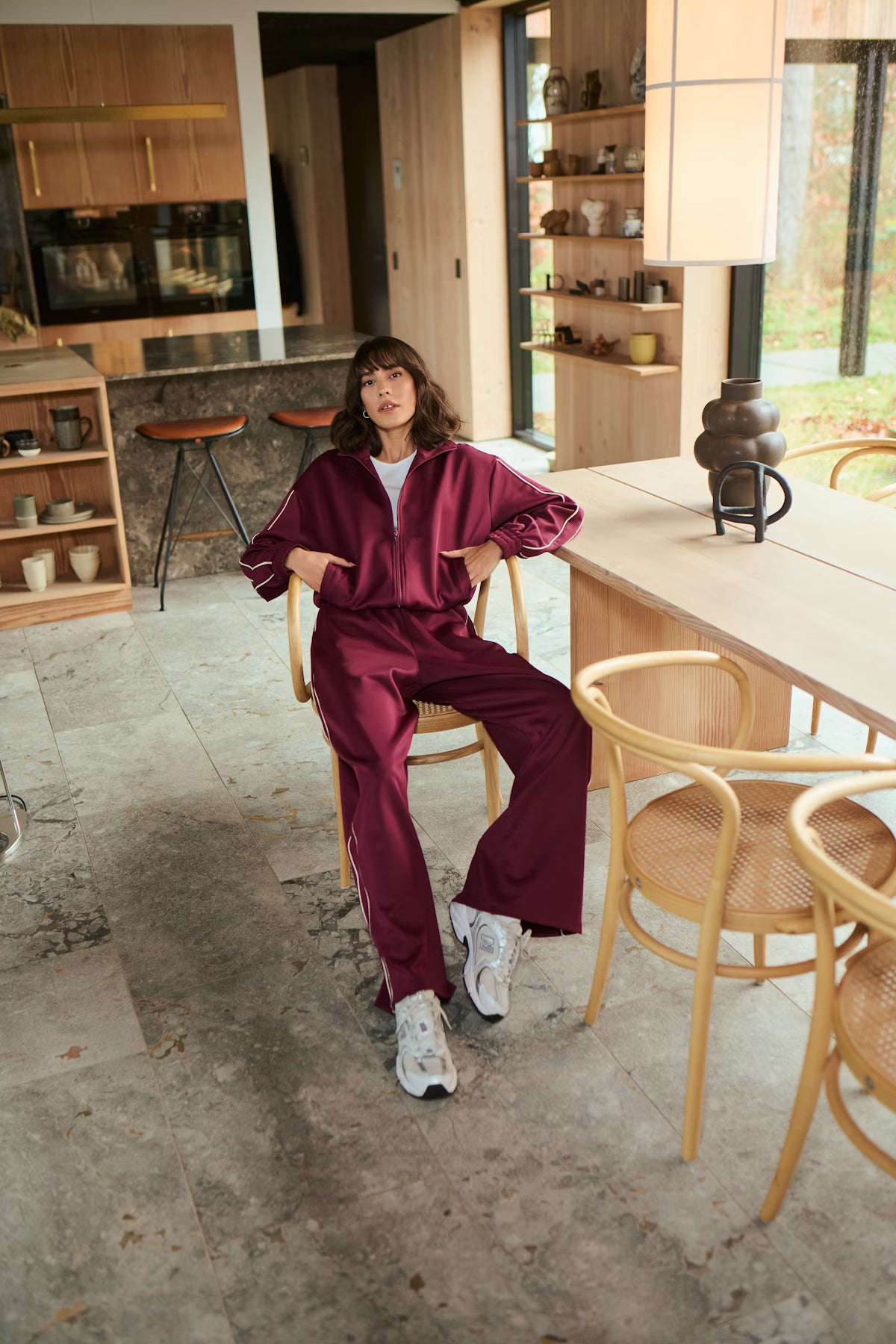 Woman in a maroon tracksuit sitting on a chair in a modern kitchen.