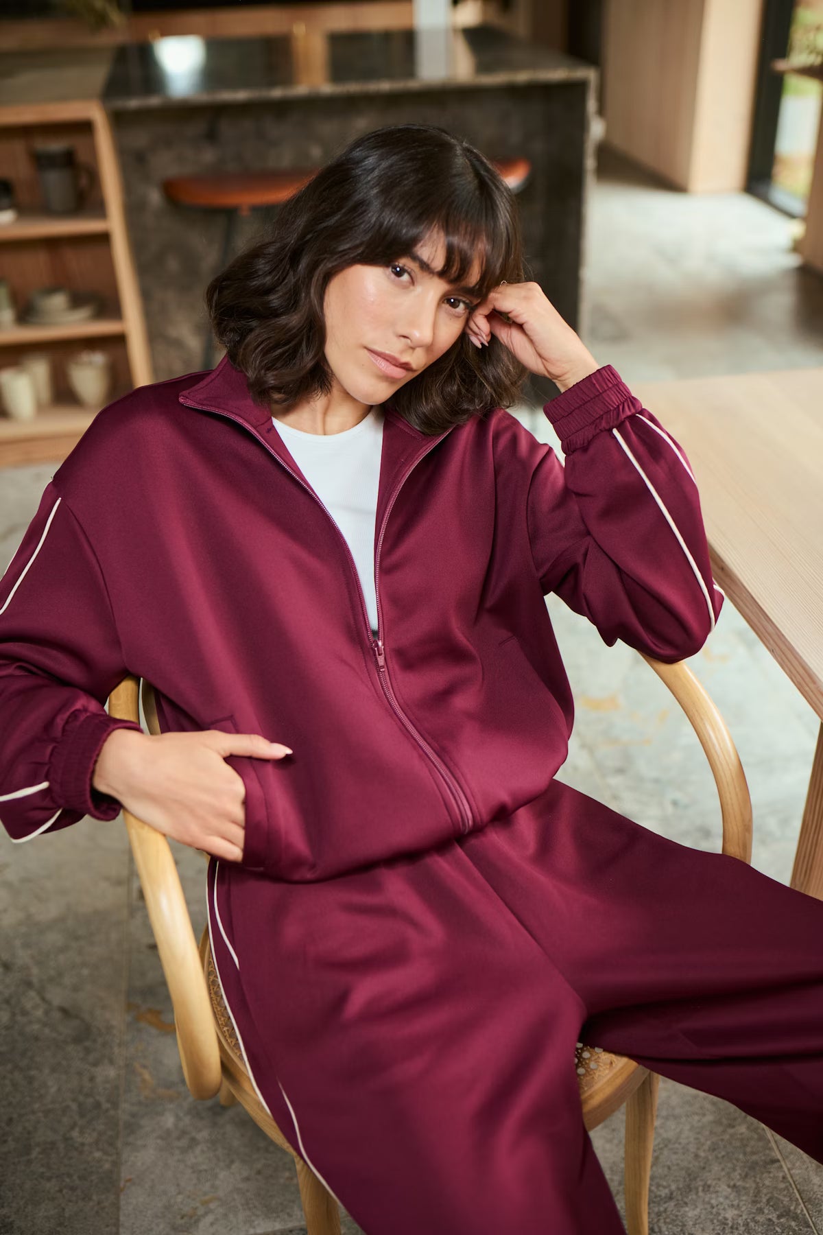 Woman wearing a maroon tracksuit sitting on a chair indoors.