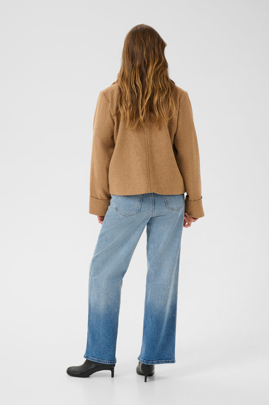 Person wearing a beige jacket and blue jeans on a white background