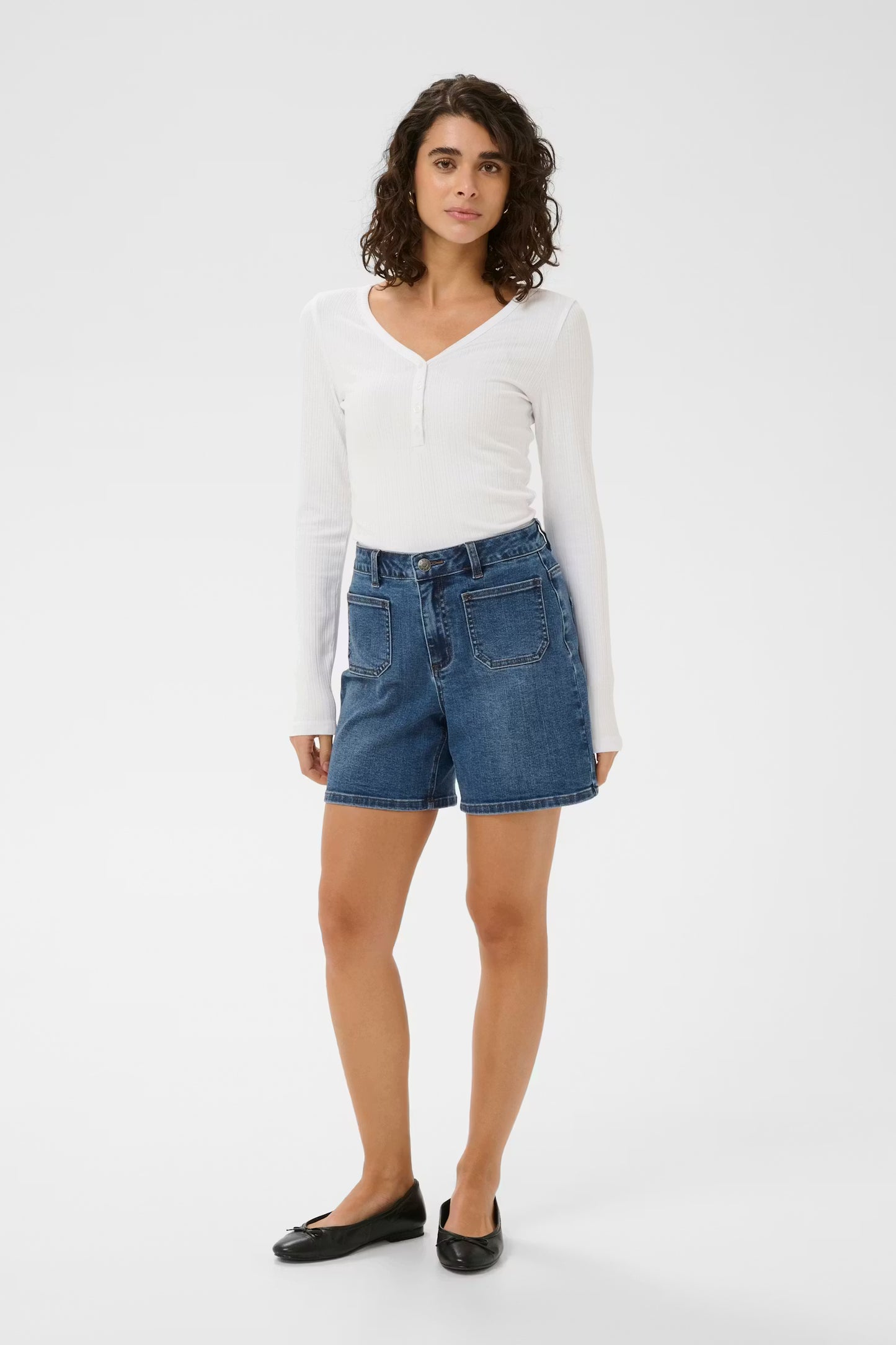 Woman wearing a white long-sleeve top and blue denim shorts on a white background