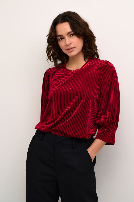 Woman wearing a red ribbed sweater and black pants against a white background