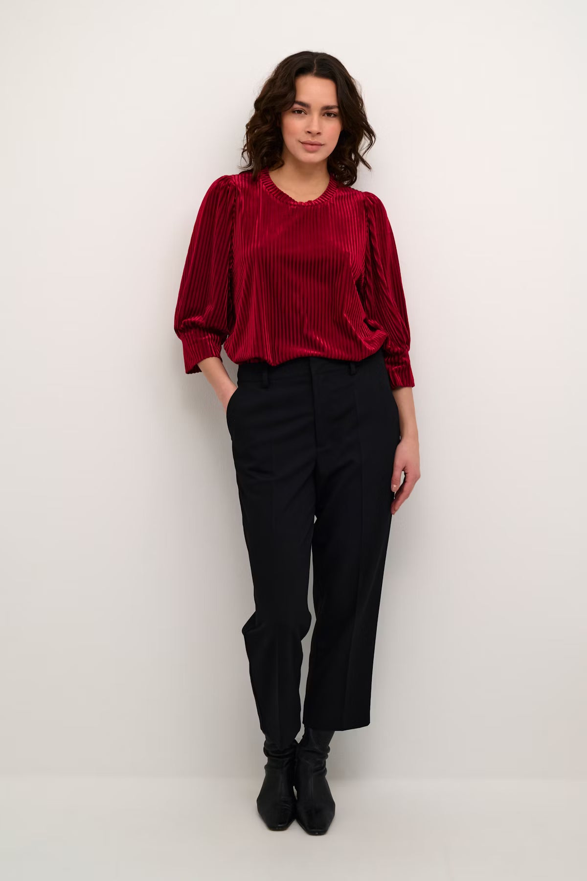Woman wearing a red blouse and black pants against a white background
