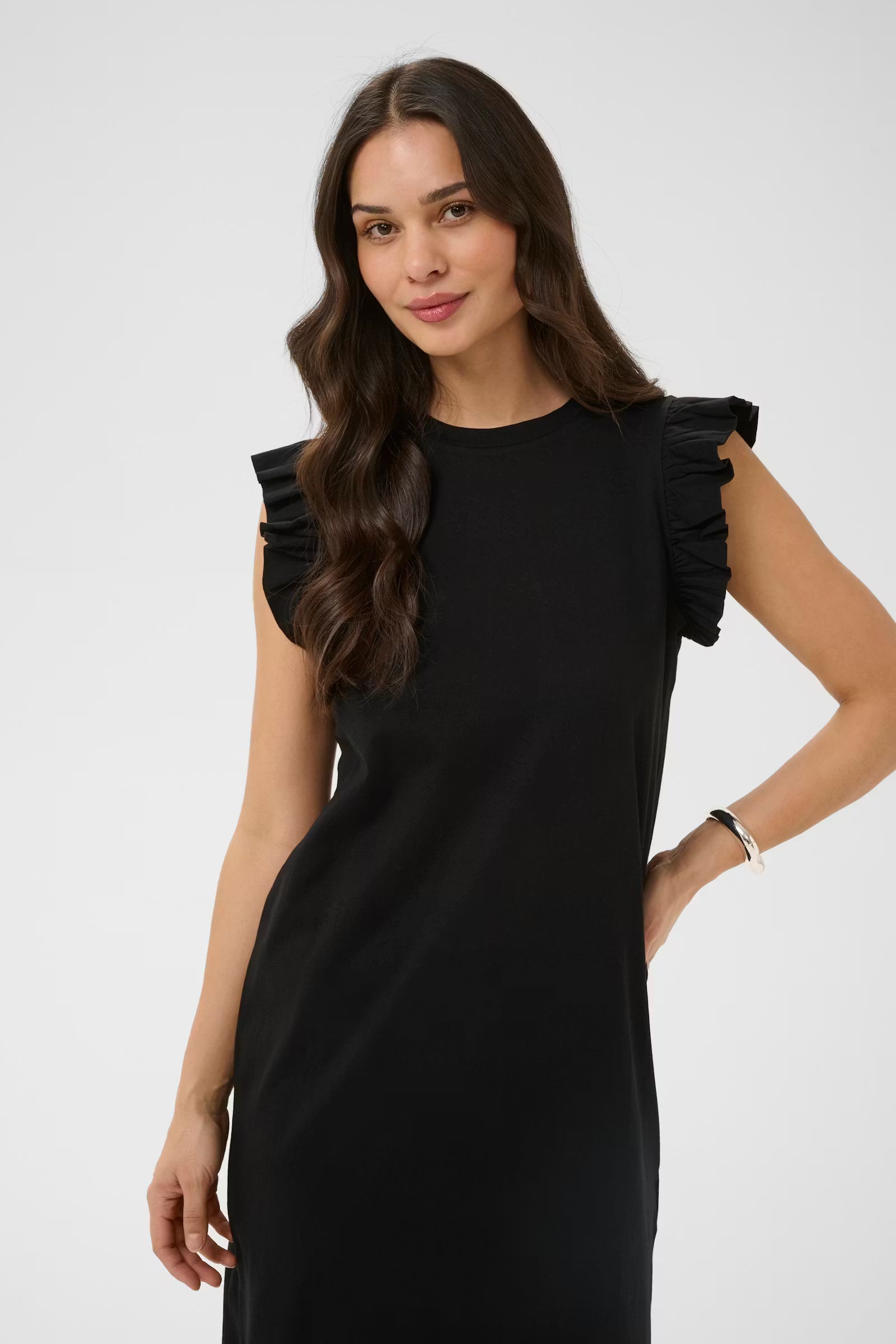 Woman wearing a black dress with ruffled shoulders against a white background