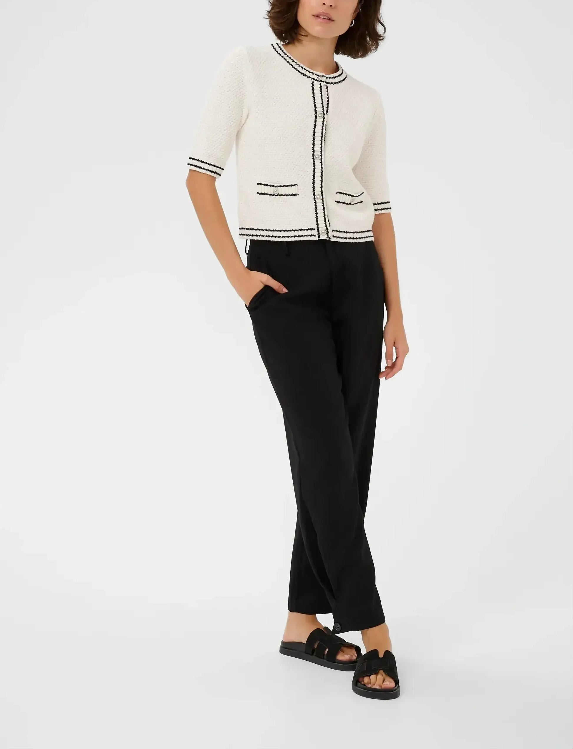 Person wearing a white cardigan with black trim and black pants on a white background