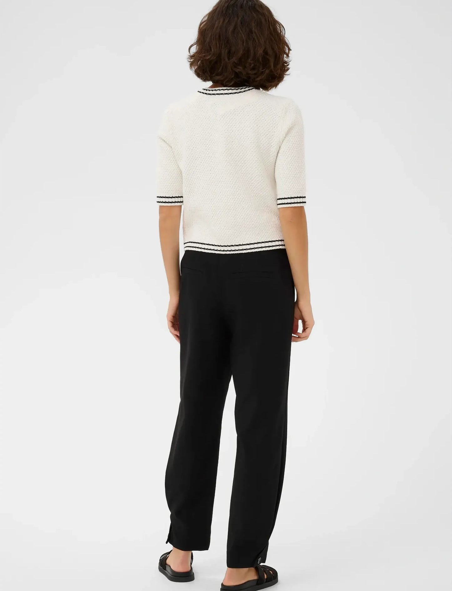 Person wearing a white sweater with black trim and black pants on a white background