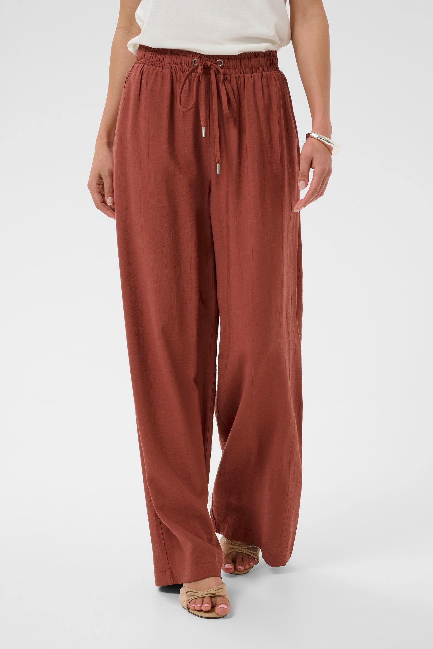 Person wearing rust-colored wide-leg pants on a white background