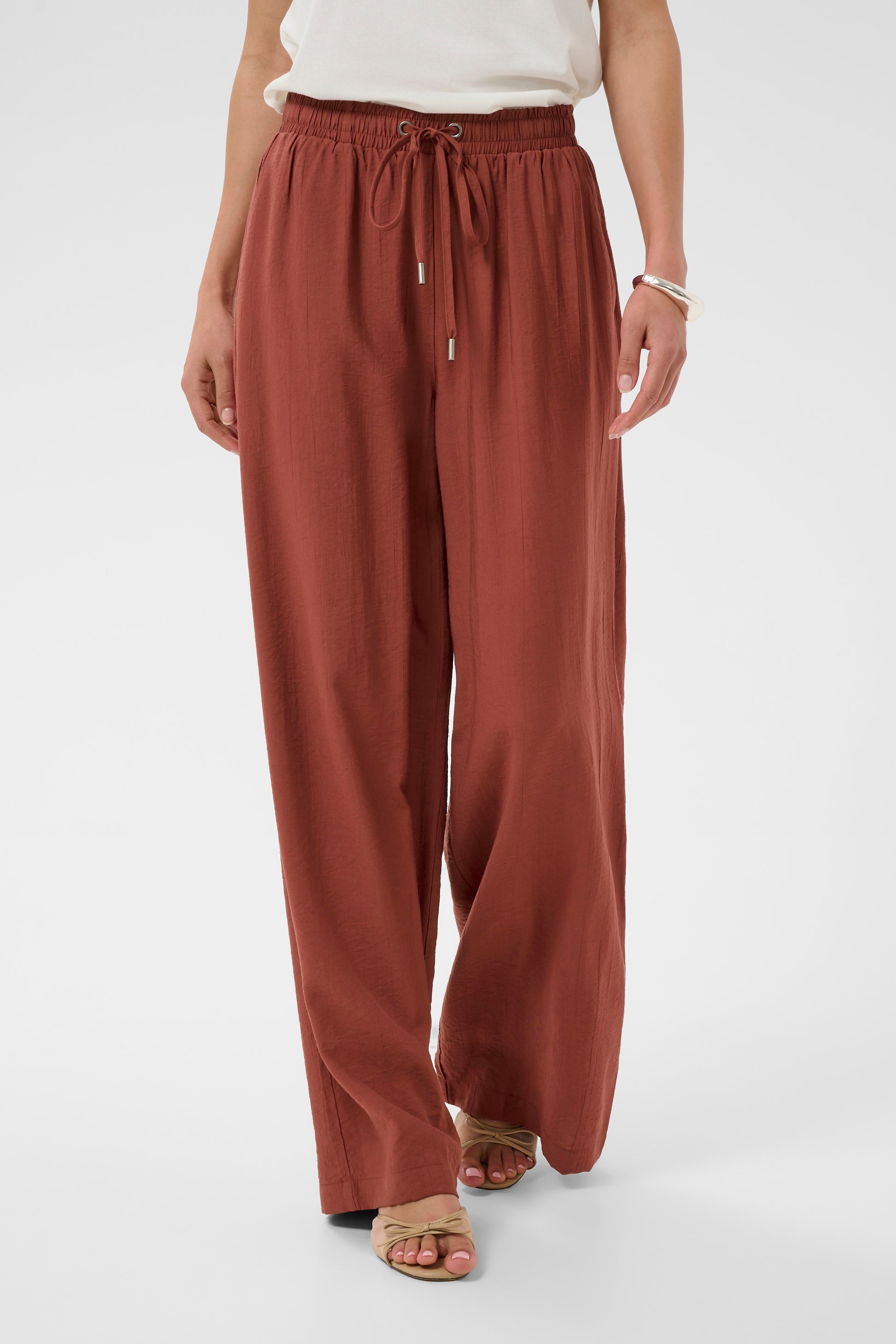Person wearing rust-colored wide-leg pants on a white background
