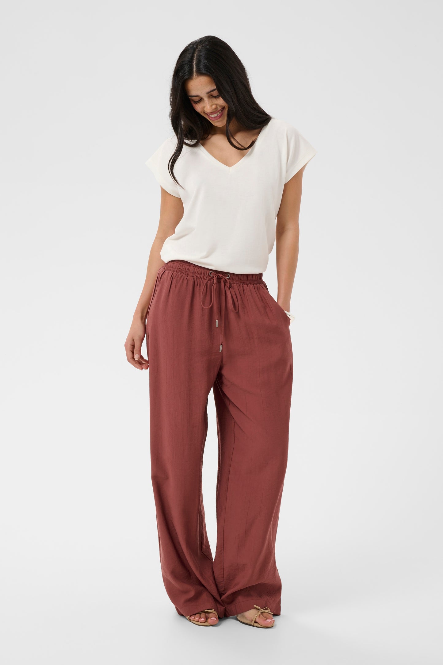 Woman wearing a white top and rust-colored pants on a white background