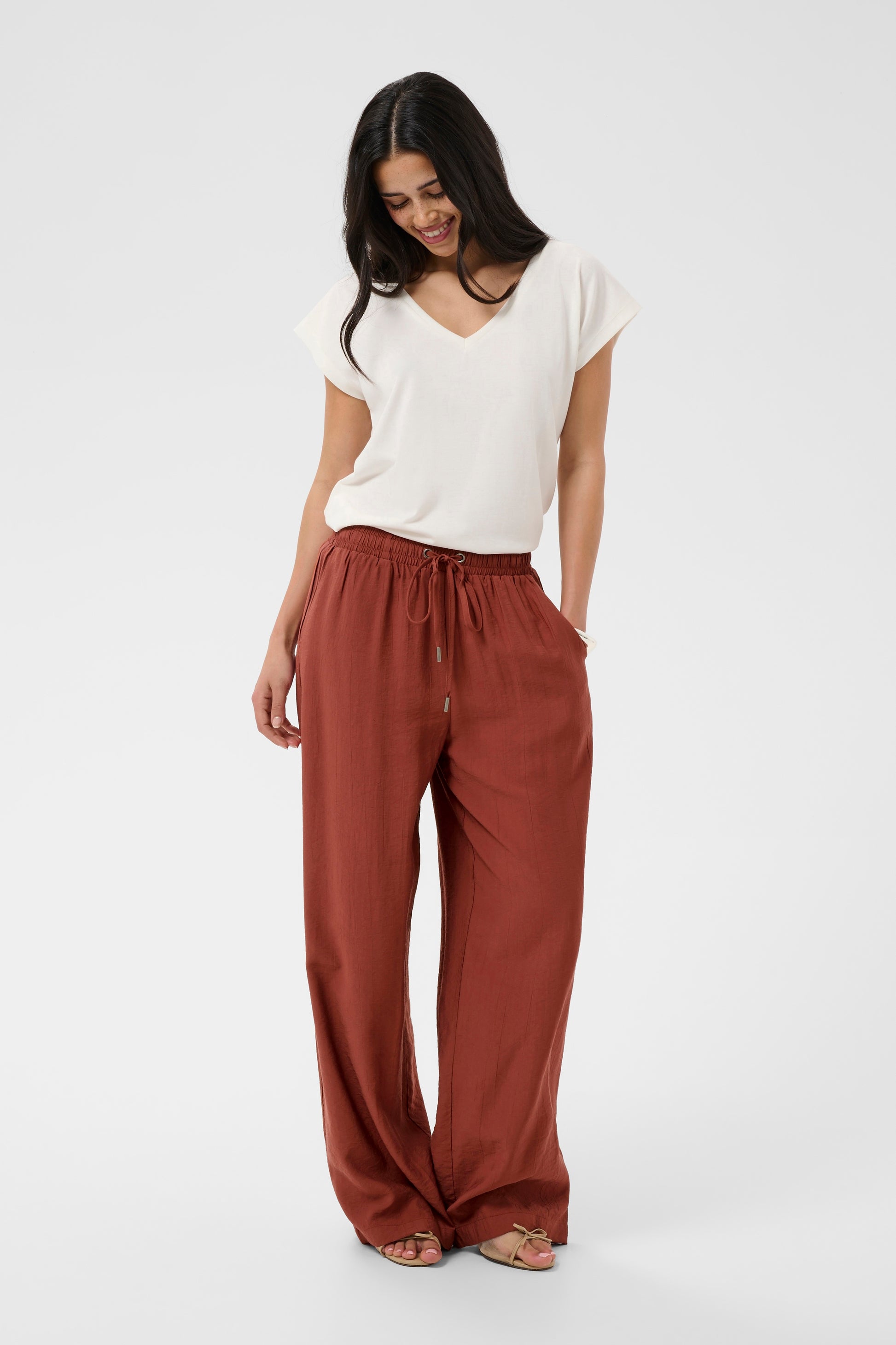 Woman wearing a white top and rust-colored pants on a white background