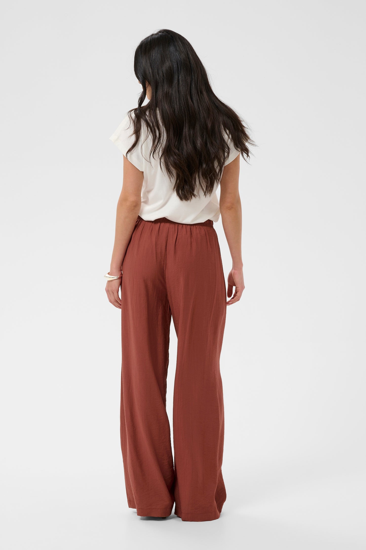 Person wearing a white top and rust-colored wide-leg pants on a white background