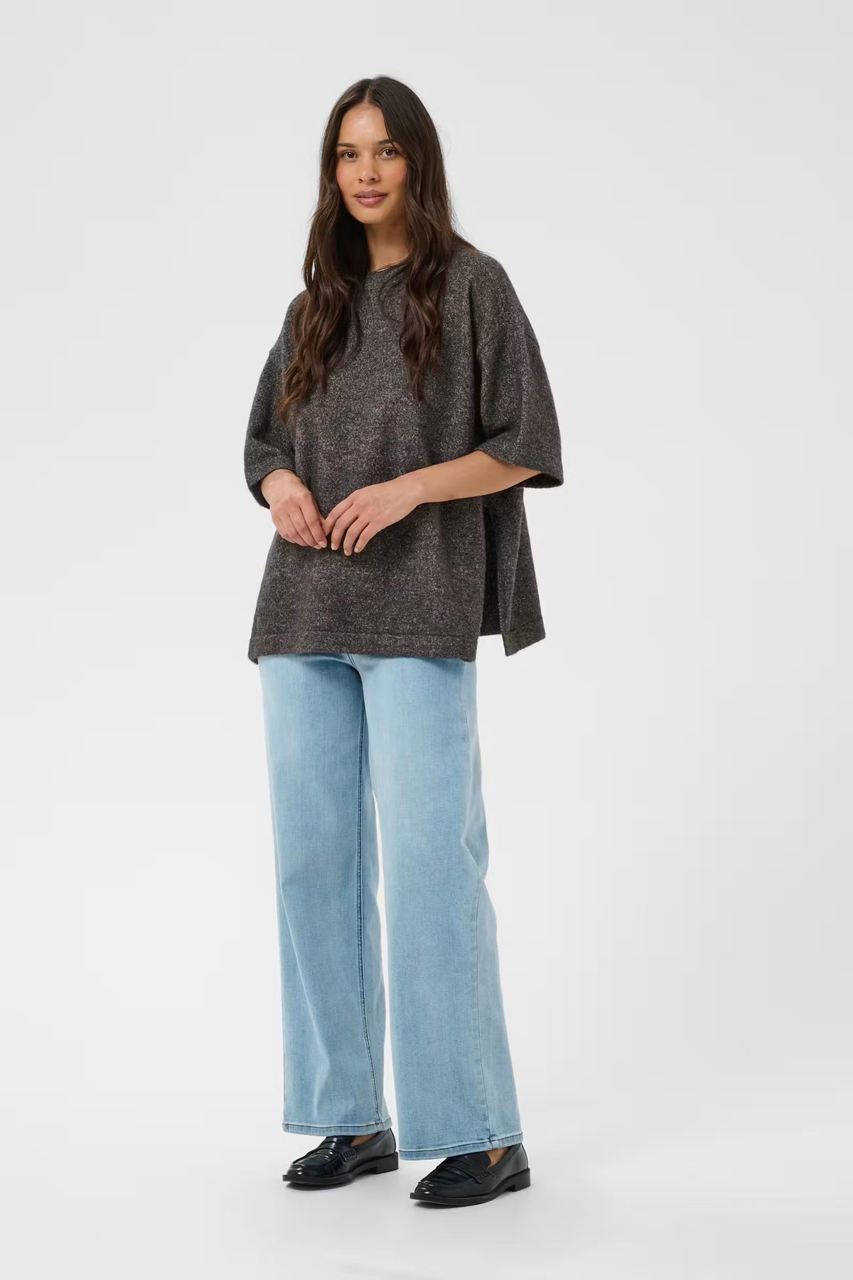 A woman modeling a dark gray textured short-sleeve top with light blue wide-leg jeans and black loafers, standing against a light gray studio background.