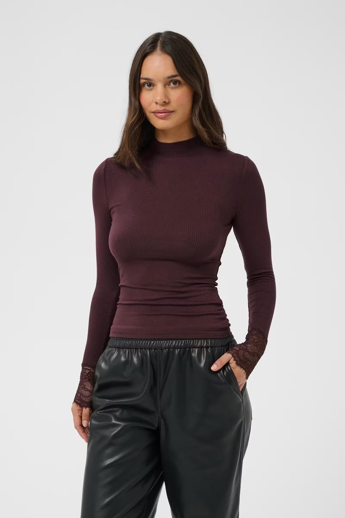 A woman modeling a fitted long-sleeve mock neck top in deep burgundy, paired with black pants, against a plain light gray studio background.