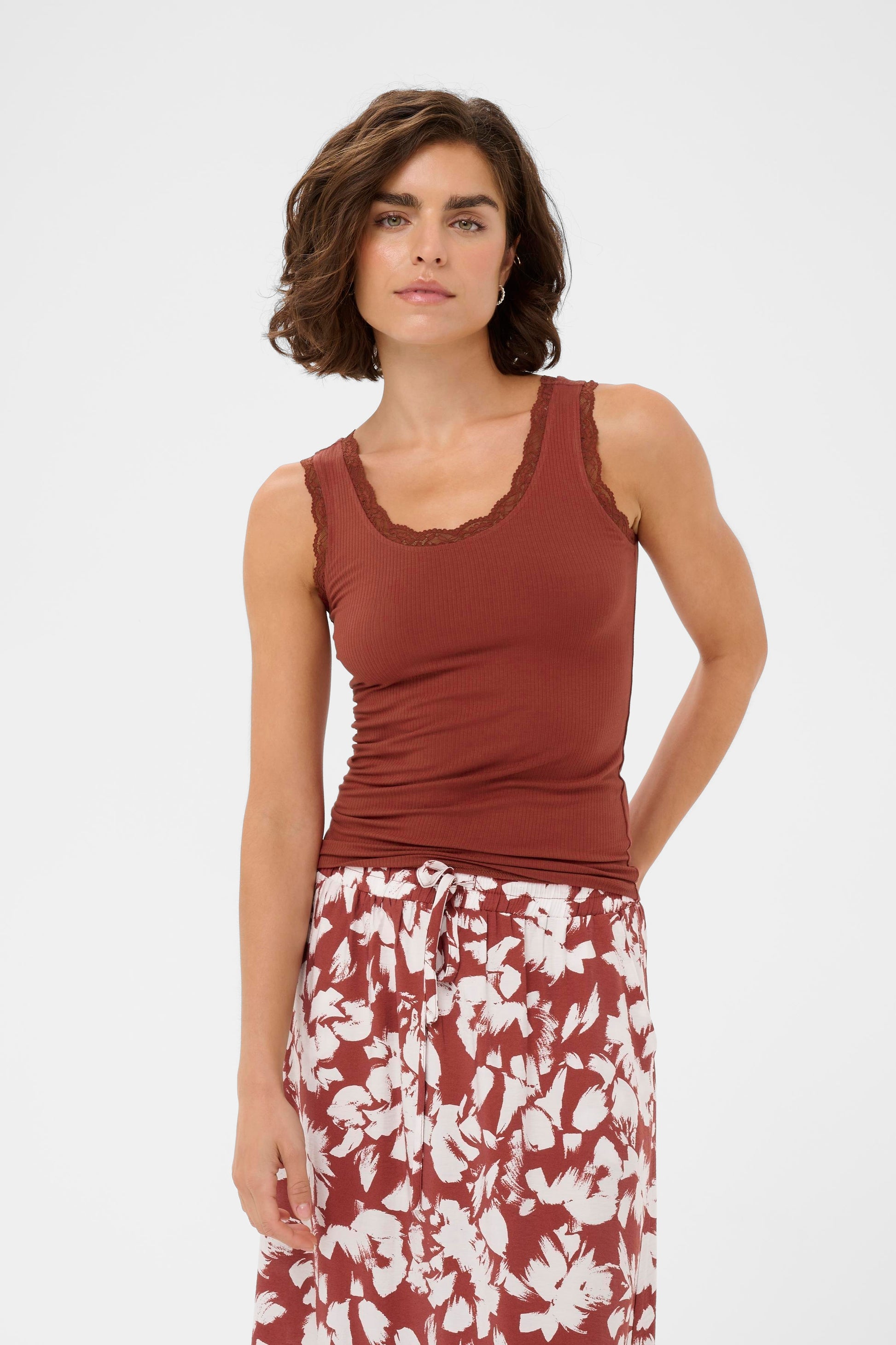 Woman wearing a rust-colored tank top and floral skirt on a white background
