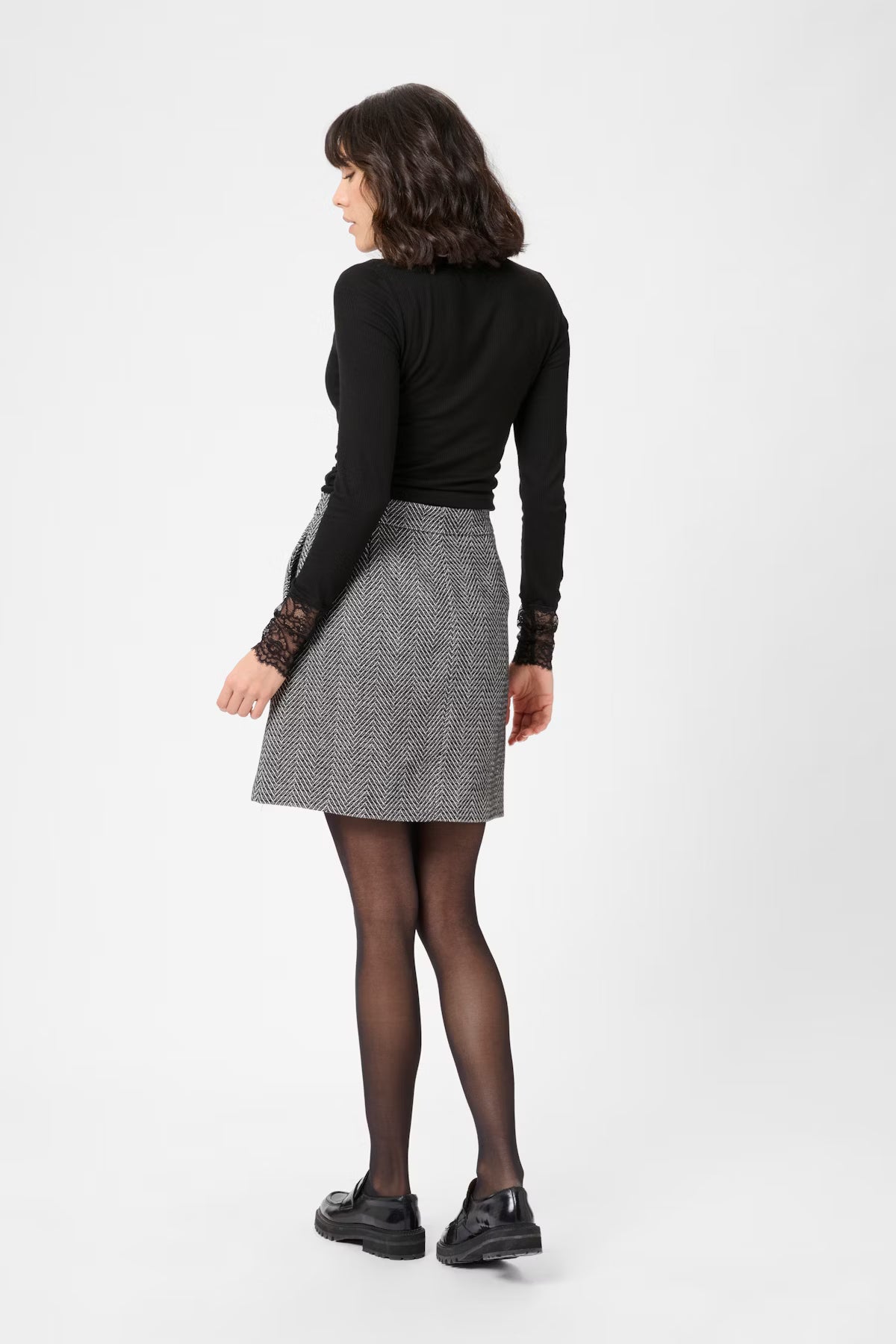 Woman wearing a black long-sleeve top and gray checkered skirt on a white background