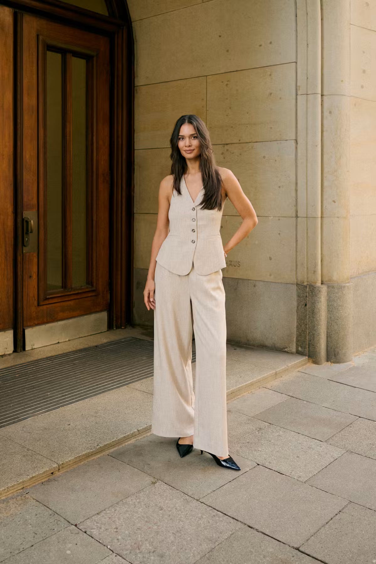 Woman in a beige suit standing in front of a building entrance.