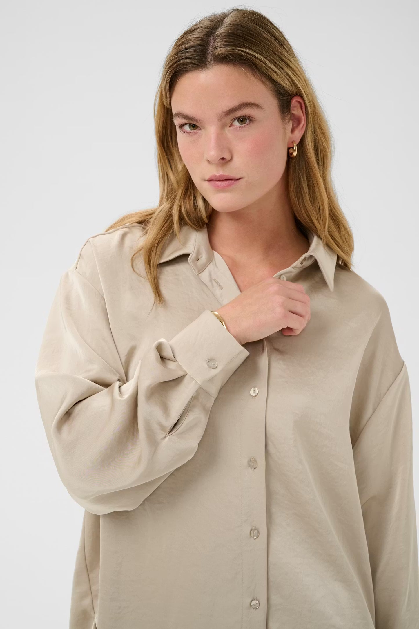 Woman wearing a beige button-up shirt against a white background
