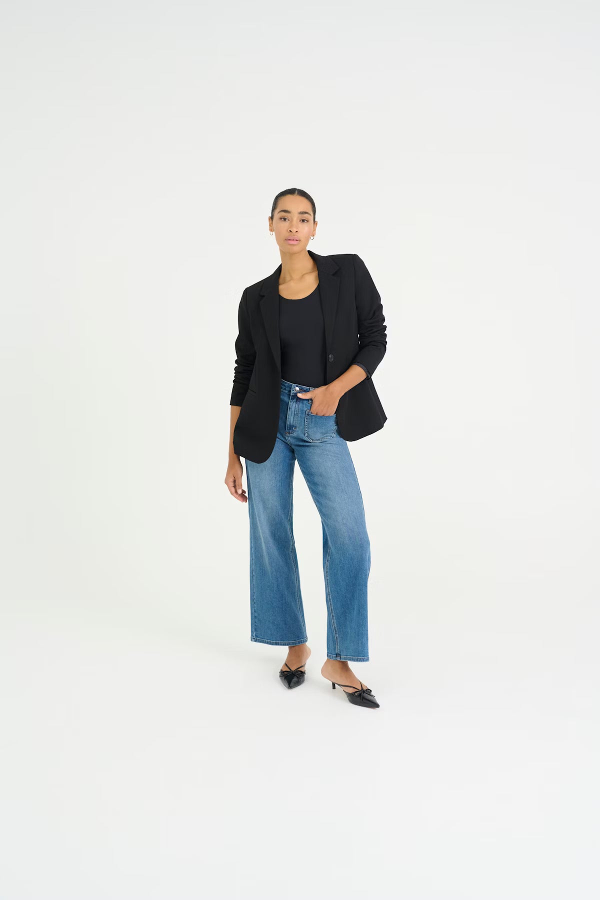Woman wearing a black blazer and blue jeans on a white background