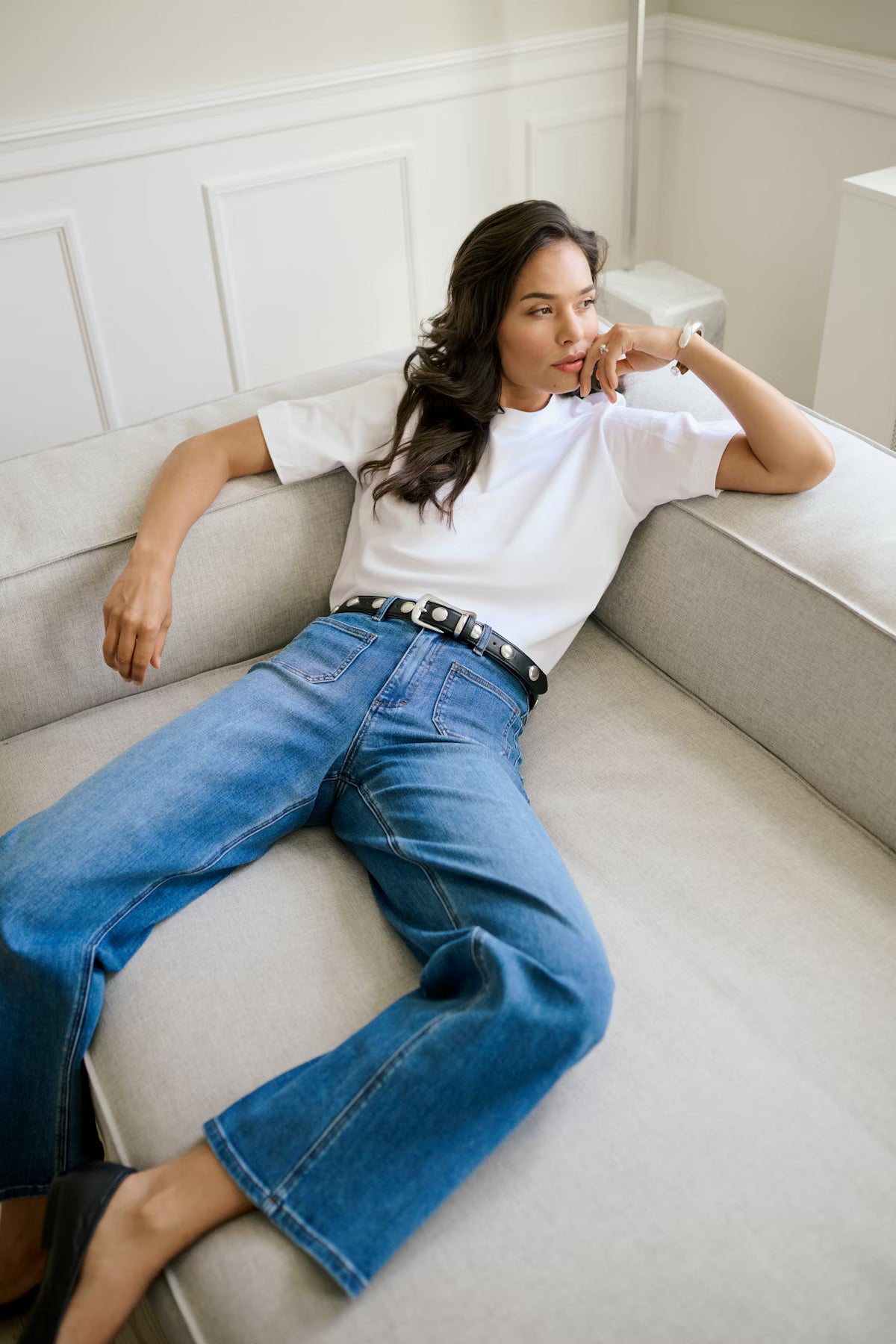 Woman wearing a white t-shirt and blue jeans sitting on a light gray sofa.