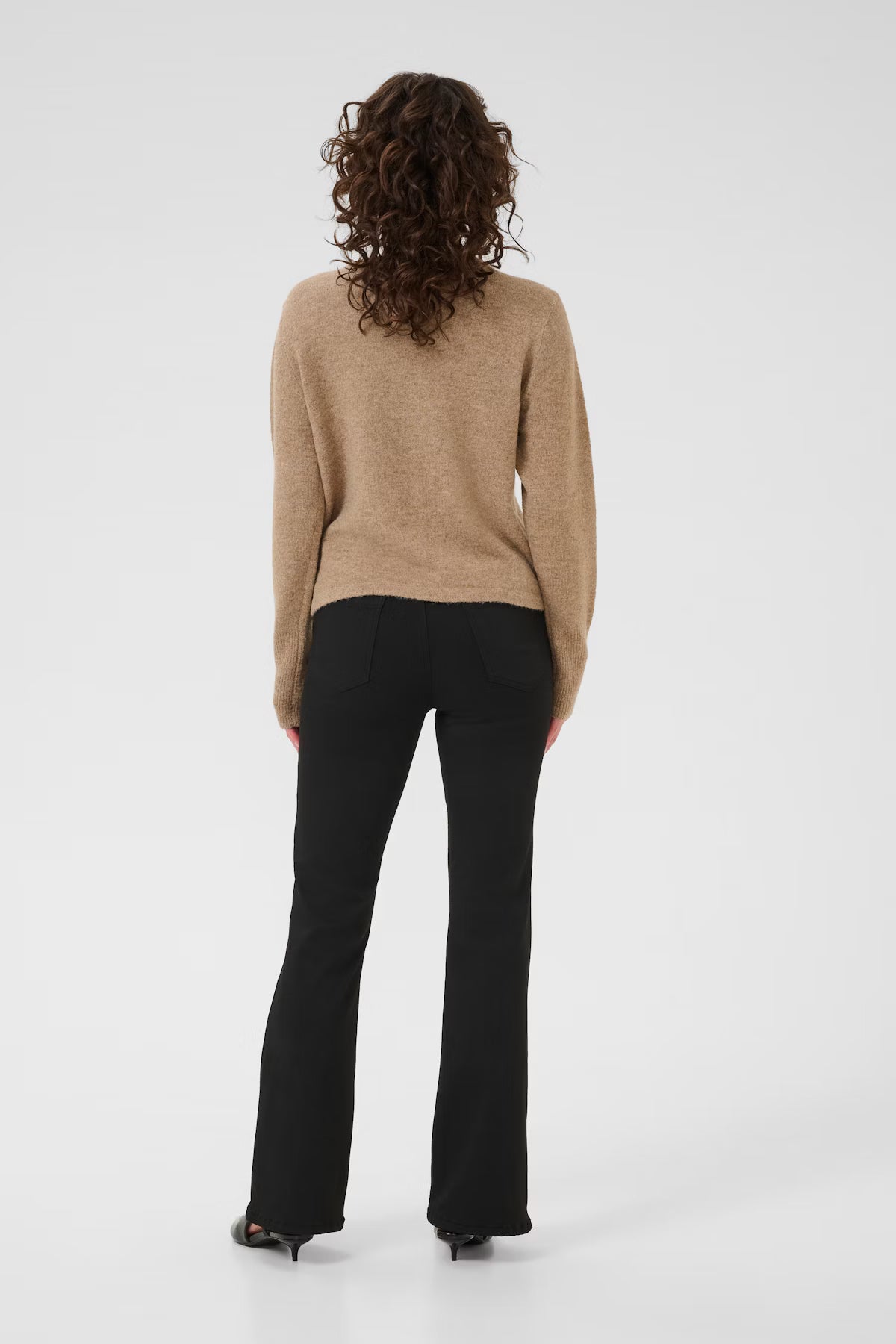 Person wearing a beige sweater and black pants on a white background