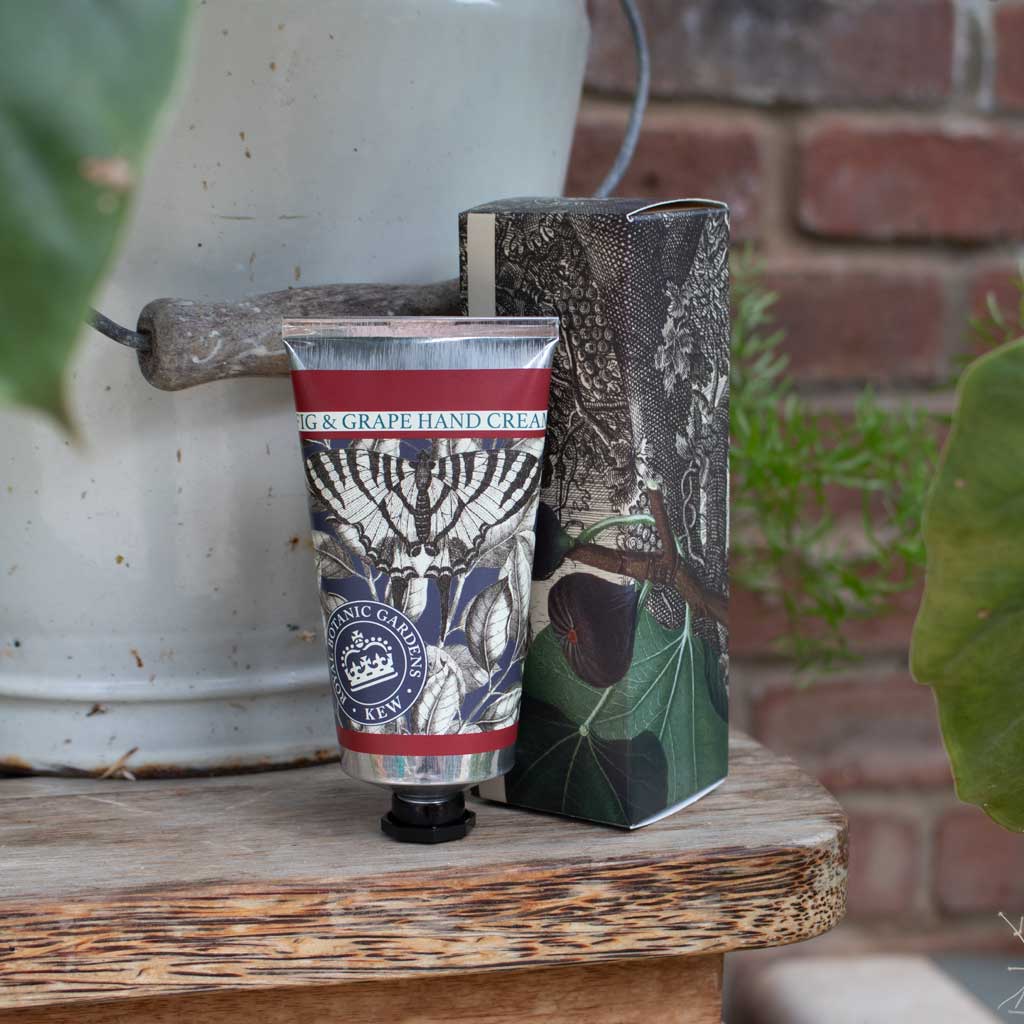 Hand cream tube with packaging on a wooden surface with plants and a brick wall in the background