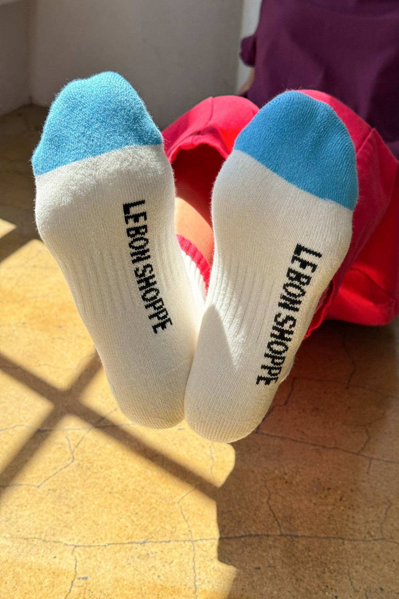 White socks with blue toes and 'LEBON SHOPPE' branding on a wooden floor.