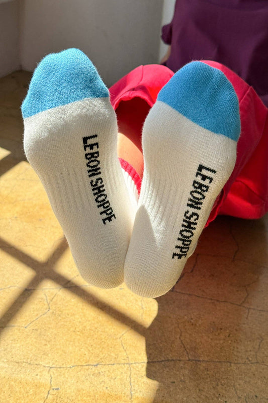 White socks with blue toes and 'LEBON SHOPPE' branding on a wooden floor.