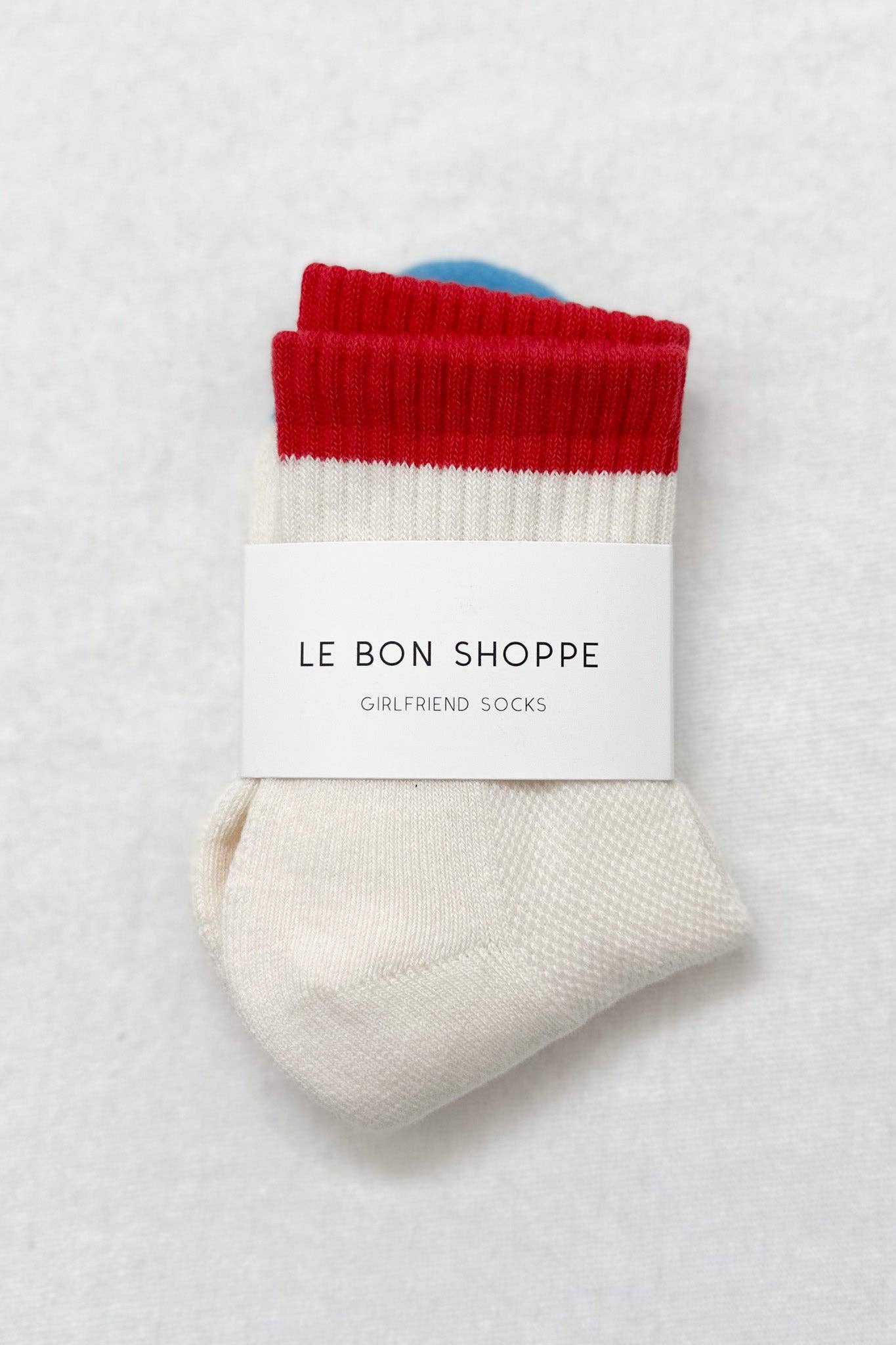 Pair of socks with red top and white bottom on a light gray background, featuring 'Le Bon Shoppe' label.