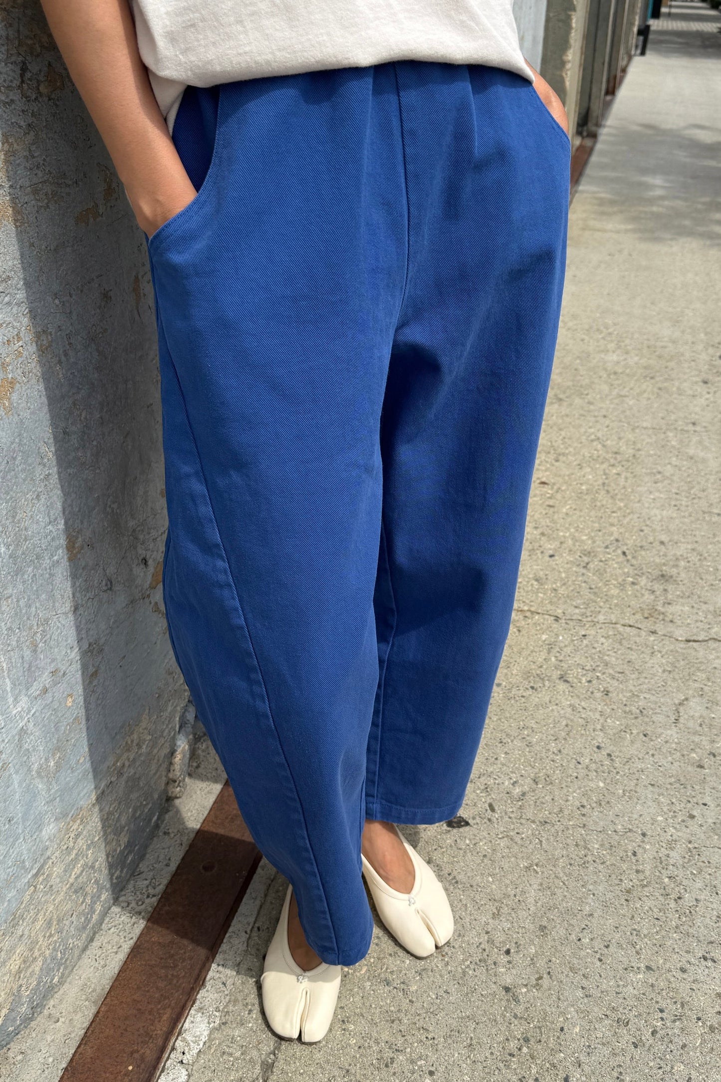 Person wearing blue pants and white shoes standing against a wall.