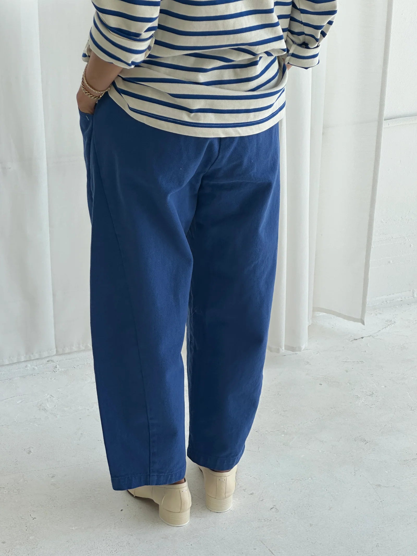 Person wearing a striped shirt and blue pants standing against a white background