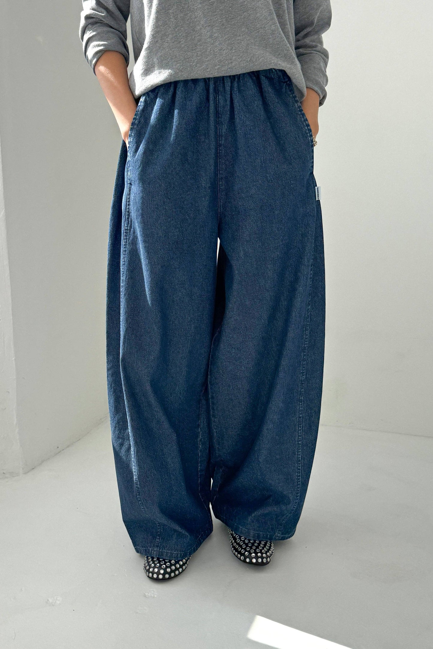 Person wearing blue wide-leg pants and a gray top on a white background