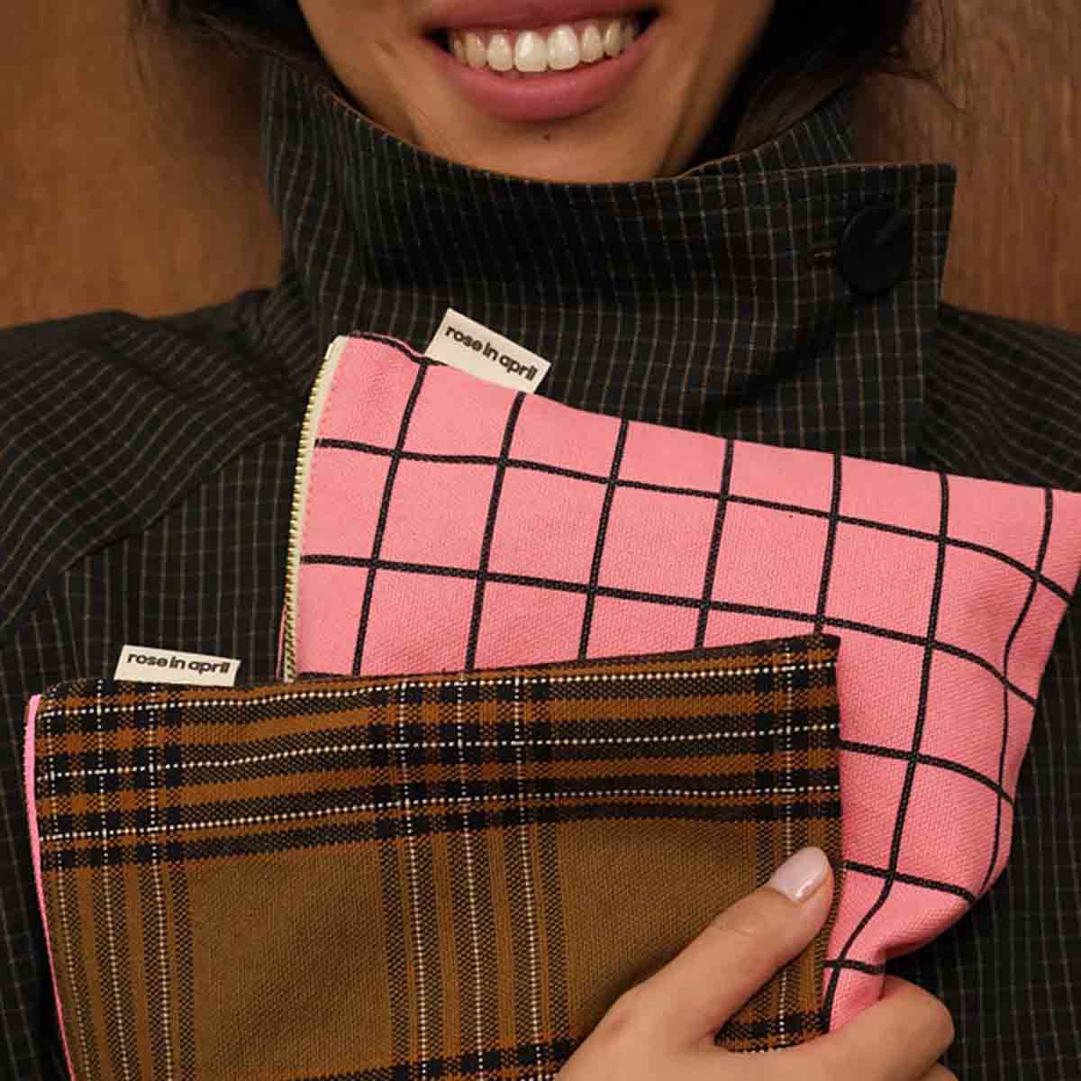 Person holding a pink checkered and plaid pouch with 'rose in april' label.