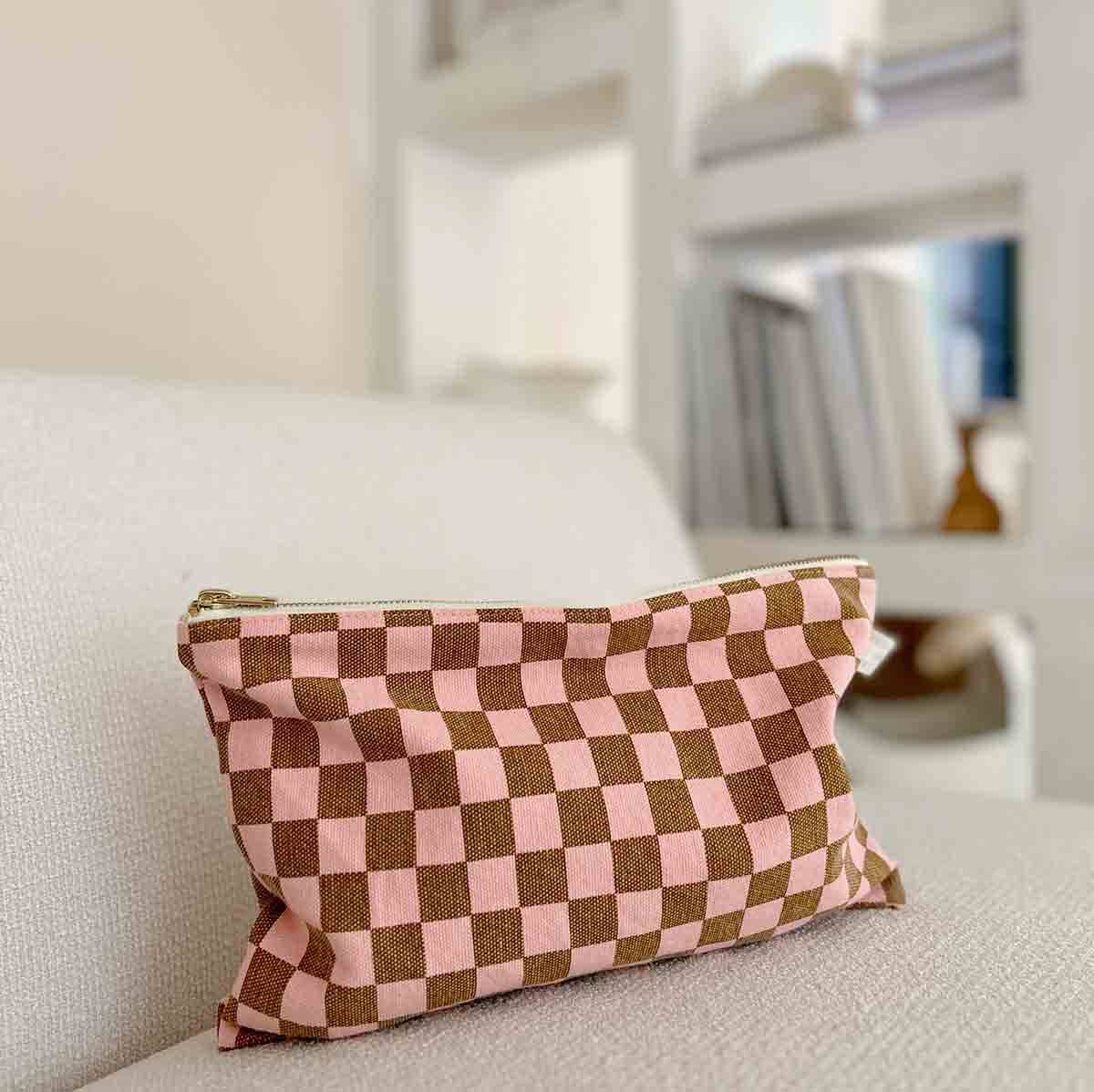 Checkered pink and brown pouch on a light-colored sofa with a blurred background
