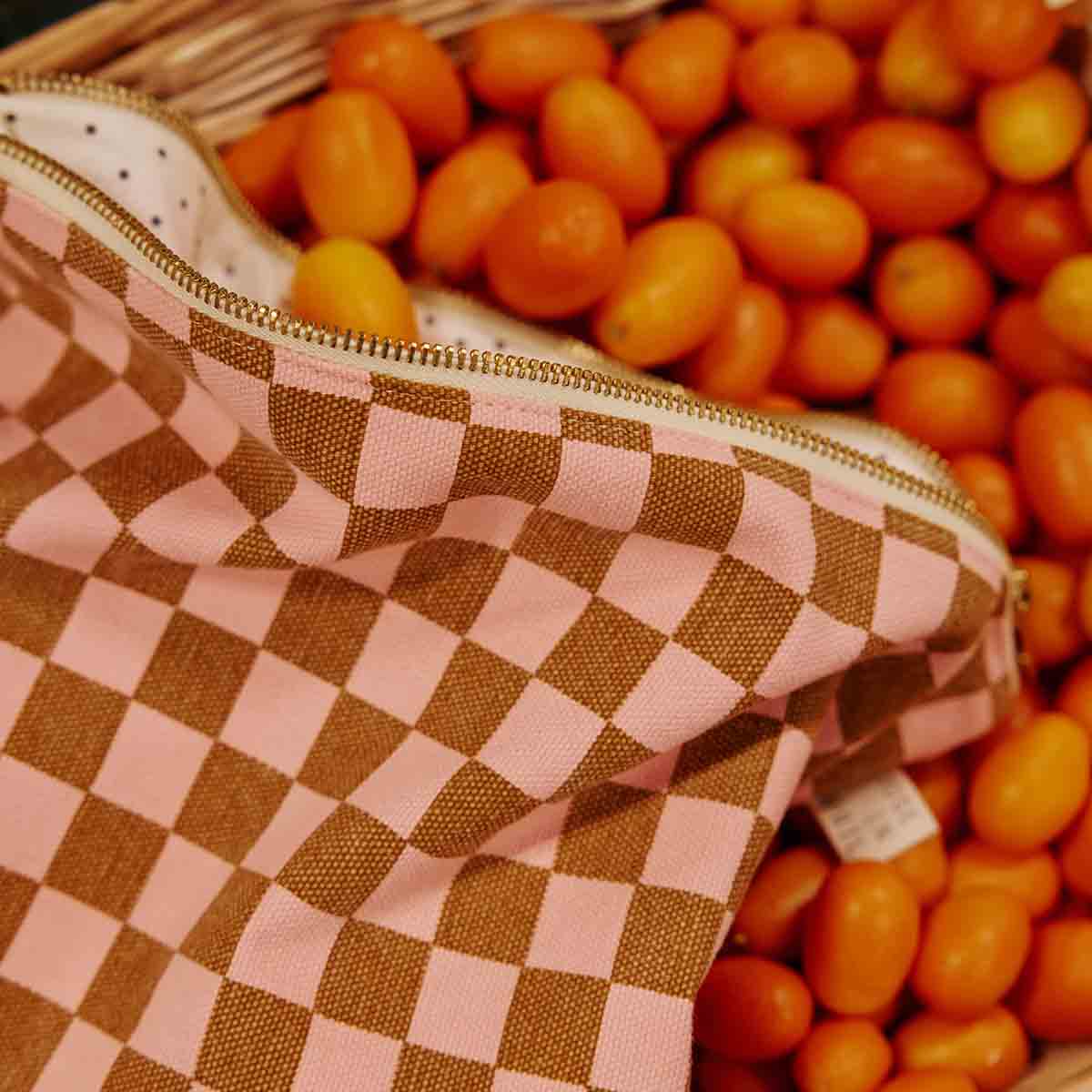 Pink and brown checkered bag with a basket of oranges in the background