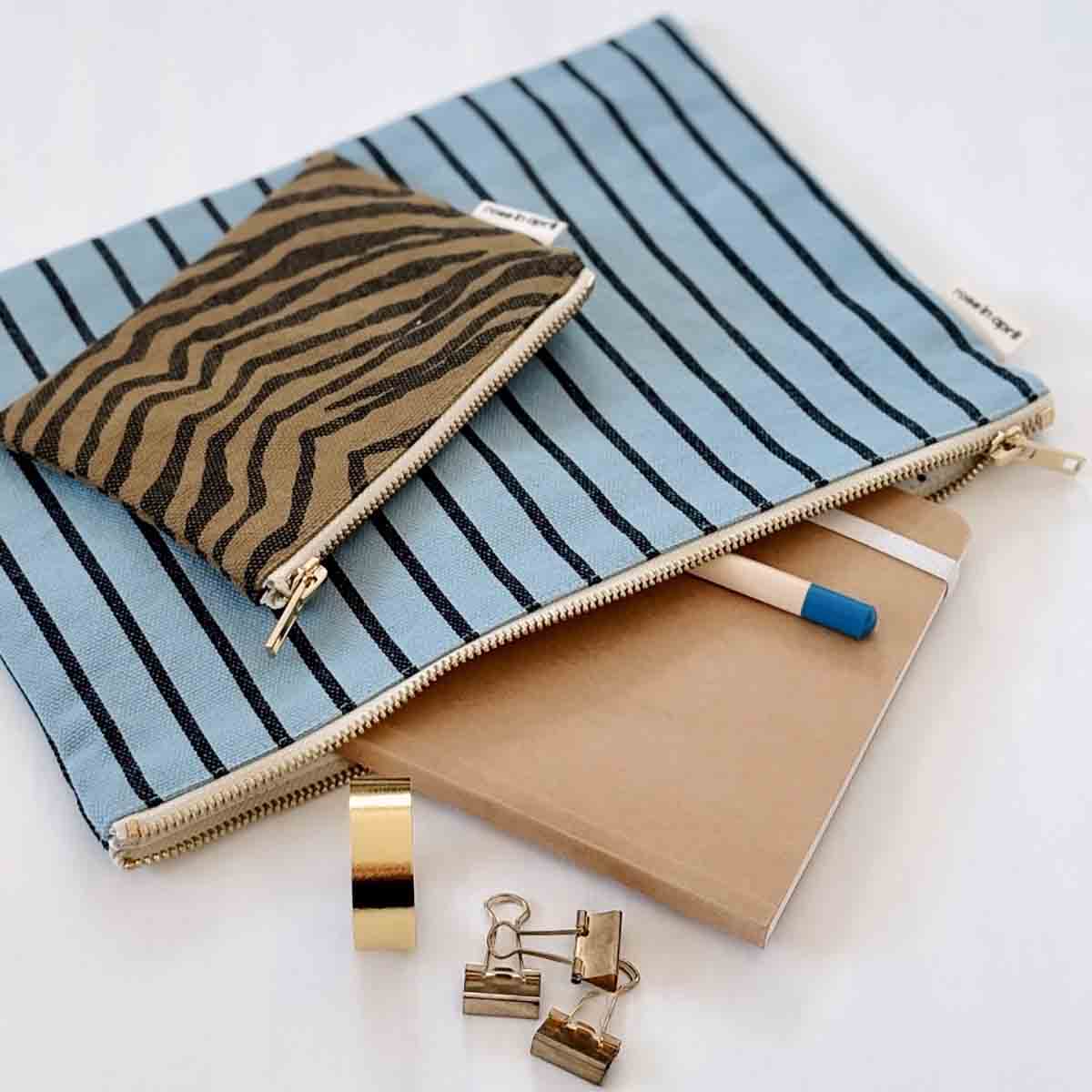 Blue striped pouch with gold zipper, tiger-striped pouch, notebook, pen, and clips on a white background