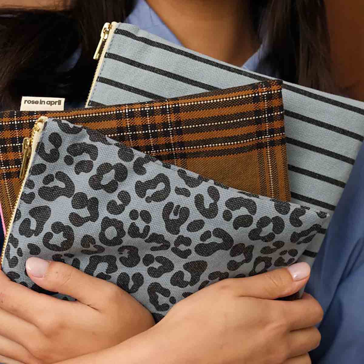 Person holding a set of patterned pouches including leopard print, plaid, and striped designs.