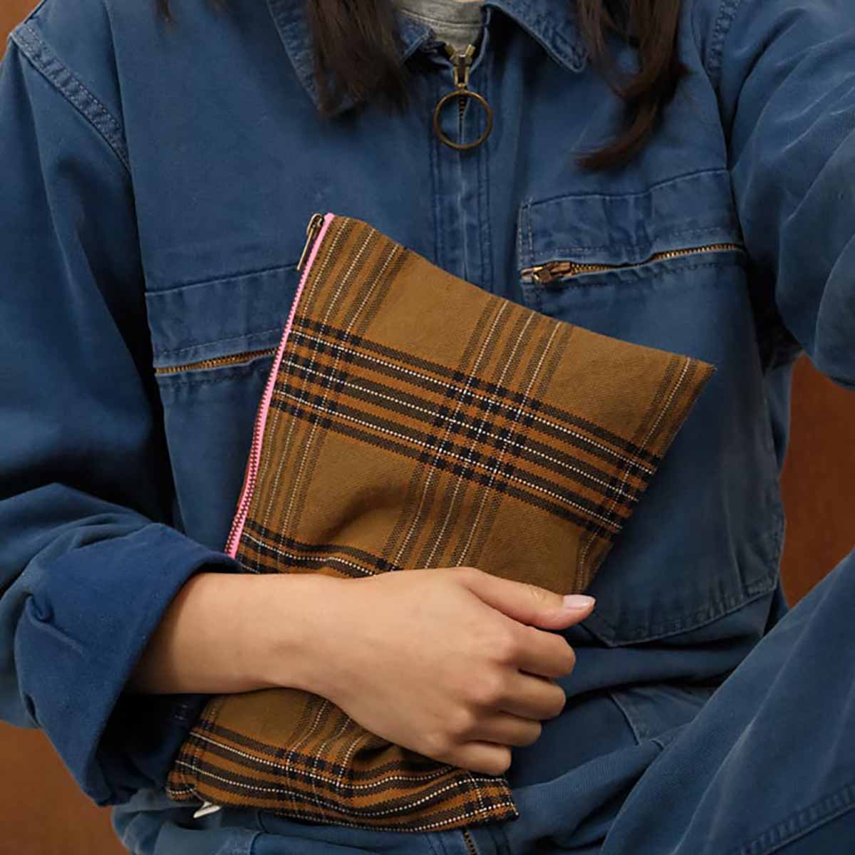 Person holding a brown plaid bag with a blue jacket