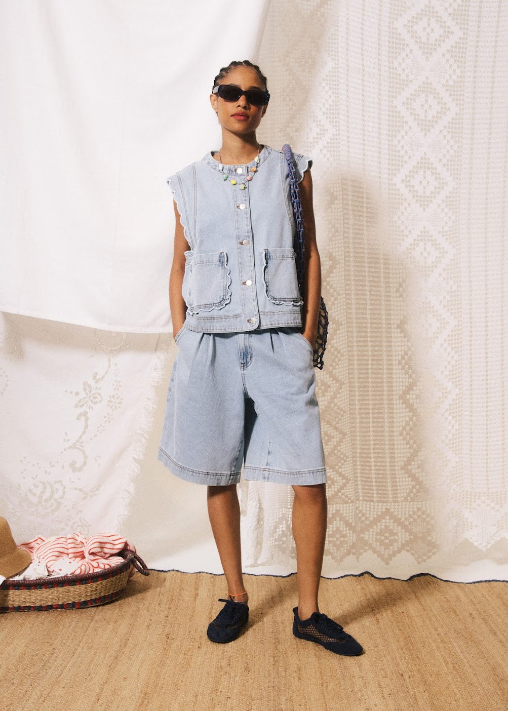 Person wearing a denim outfit with sunglasses against a textured white wall.