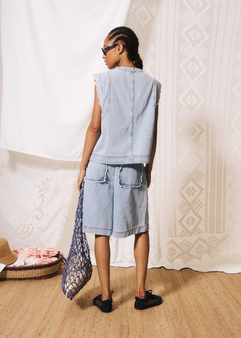 Person wearing a denim outfit standing in a room with a textured white wall.