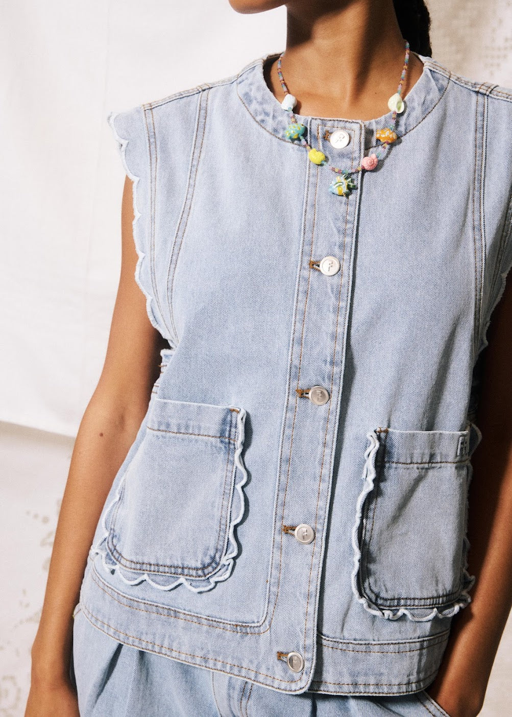 Denim vest with decorative buttons and ruffled edges worn by a person.