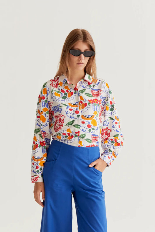 Woman wearing a colorful floral blouse and blue pants on a light gray background