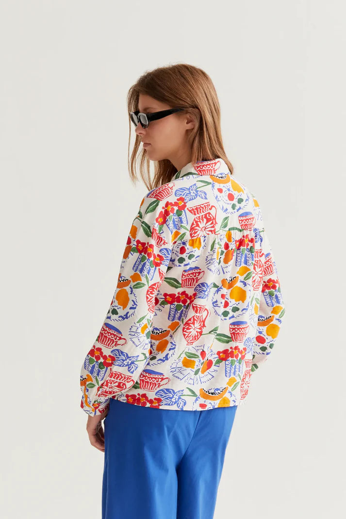 Woman wearing a colorful patterned shirt and blue pants on a white background