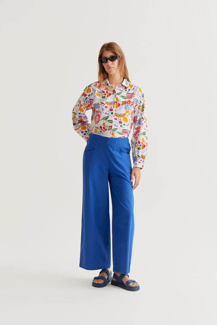 Person wearing a colorful floral shirt and blue pants on a white background