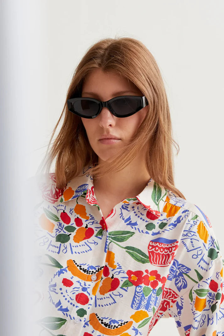Woman wearing a colorful patterned shirt with sunglasses on a white background
