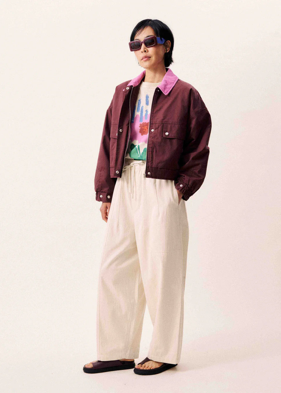 Person wearing a maroon jacket, colorful shirt, and beige pants on a white background