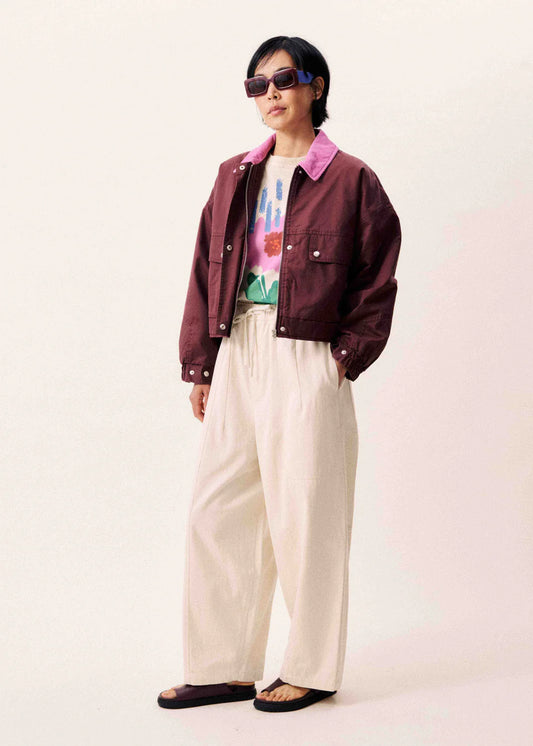 Person wearing a maroon jacket, colorful shirt, and beige pants on a white background