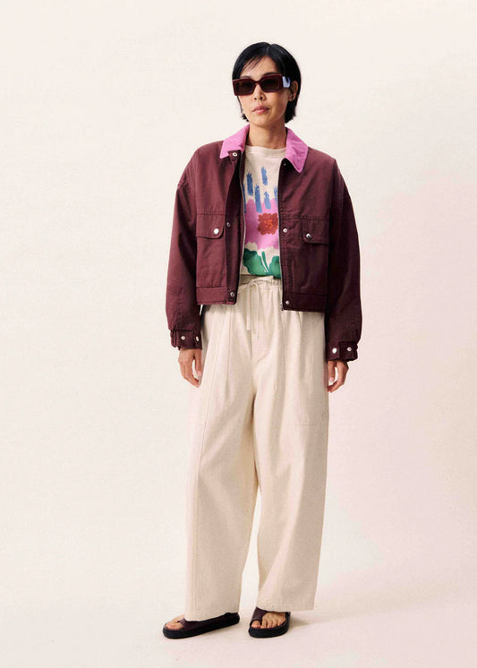 Person wearing a burgundy jacket, colorful shirt, and beige pants on a light pink background