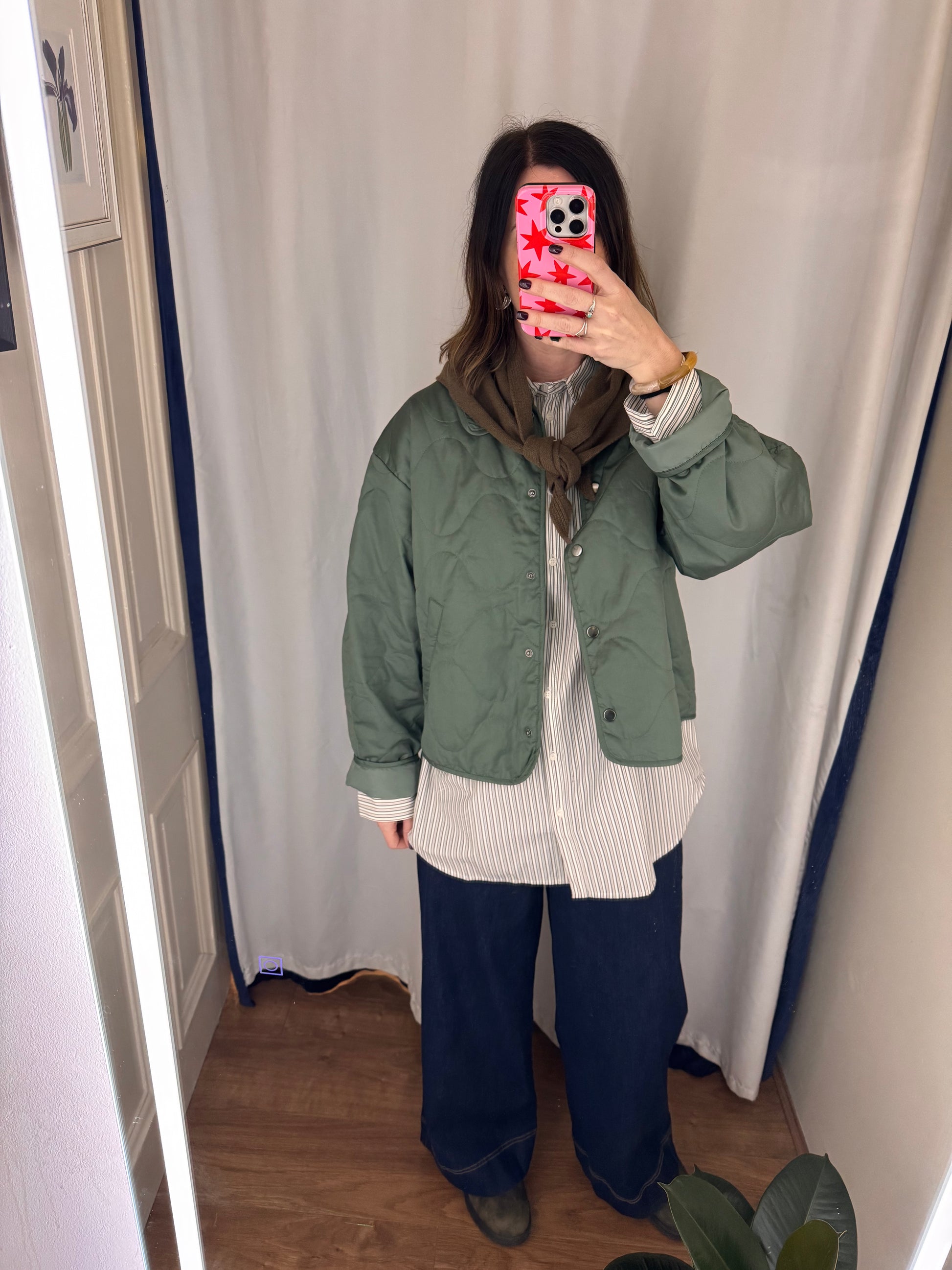 Person wearing a green jacket and blue pants taking a mirror selfie.