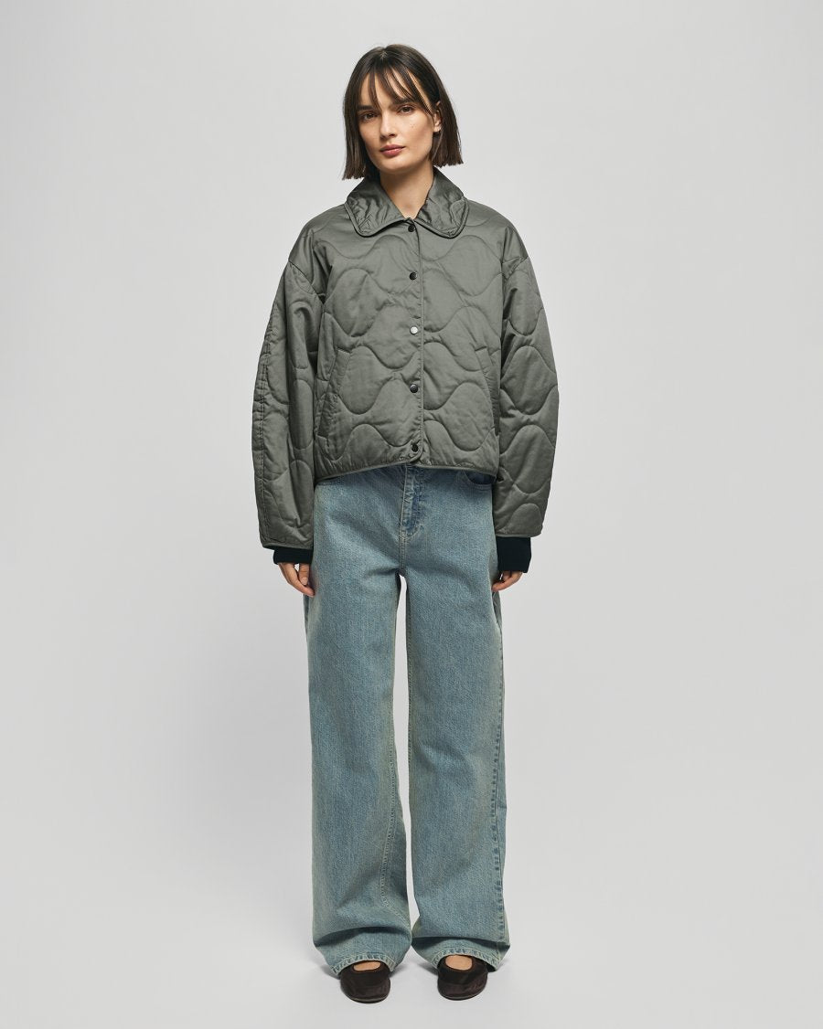 Person wearing a quilted jacket and jeans on a plain background